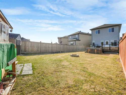 Expansive fenced backyard featuring a large grass area, a built-in fire pit, a wooden deck with glass panel railings, and a detached shed - 17171 38 Street, Edmonton, AB 