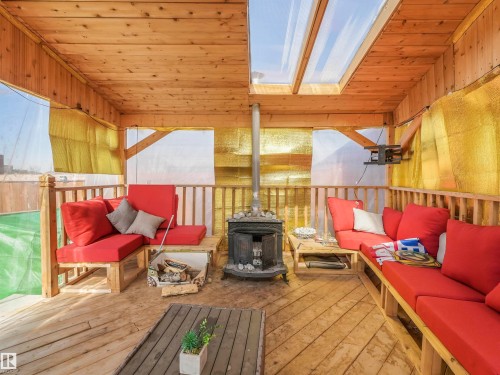 Covered outdoor patio featuring a wood-finish ceiling with skylights, wood-finish flooring, and a central wood-burning stove - 17171 38 Street, Edmonton, AB 