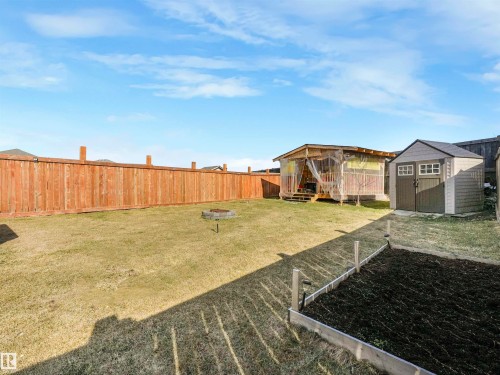Expansive backyard featuring a privacy fence, a raised garden bed, a fire pit, a storage shed, and a covered deck structure - 17171 38 Street, Edmonton, AB 