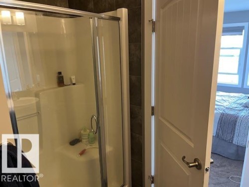 Walk-in shower with clear glass enclosure and integrated shelving, featuring dark tile surround and a chrome-finish showerhead - 138 Reed Place, Leduc, AB 