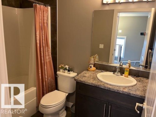 Bathroom featuring a built-in tub and shower combination, dark tiled shower surround, a vanity with an integrated sink, and a multi-bulb light fixture - 138 Reed Place, Leduc, AB 