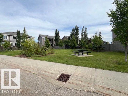 Community green space featuring a picnic table on a concrete pad, surrounded by mature trees and manicured lawn - 138 Reed Place, Leduc, AB 