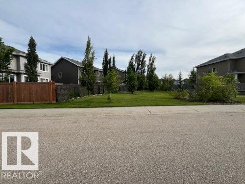 Expansive vacant lot featuring a manicured lawn, established landscaping, and mature trees - 138 Reed Place, Leduc, AB 