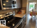 Modern kitchen featuring stainless steel appliances, dark wood-finish cabinetry, a ceramic tile backsplash, and light-toned countertop - 138 Reed Place, Leduc, AB 