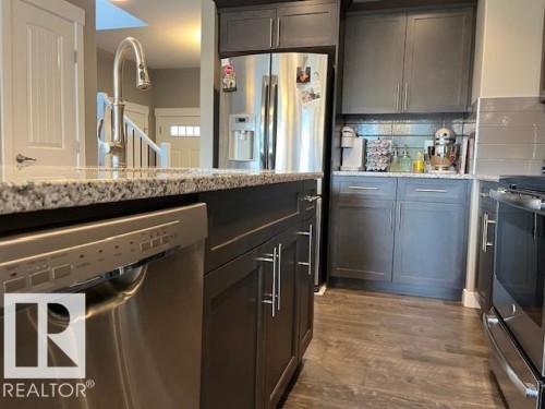 Kitchen featuring wood-finish flooring, dark cabinetry, and granite countertops - 138 Reed Place, Leduc, AB 