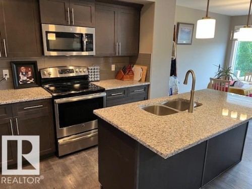 Modern kitchen featuring wood-finish flooring and dark cabinetry - 138 Reed Place, Leduc, AB 