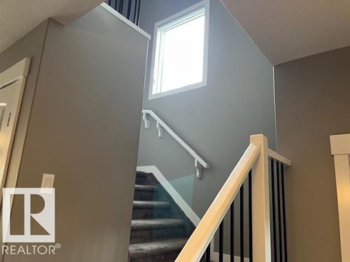 Carpeted staircase with white trim and dark balusters, illuminated by a window - 138 Reed Place, Leduc, AB 