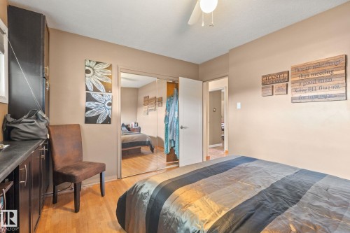 Bedroom featuring wood-finish flooring, a ceiling fan, and a built-in dark wood storage unit with a dark countertop - 12115 53 Street, Edmonton, AB 