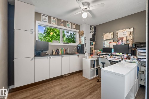 Dedicated workspace featuring extensive built-in white cabinetry, a dark countertop, and wood-finish flooring - 12115 53 Street, Edmonton, AB 