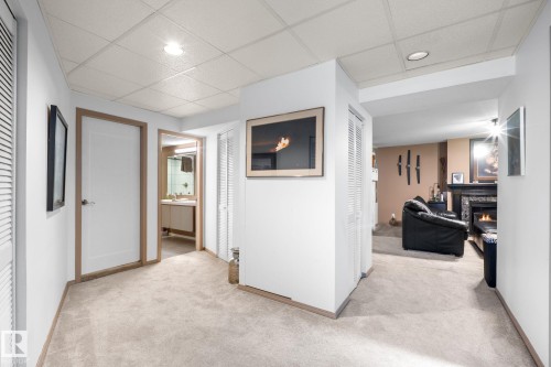 Carpeted hallway with white walls and light wood trim, featuring a recessed ceiling light, white paneled doors, and louvered closet doors - 12115 53 Street, Edmonton, AB 