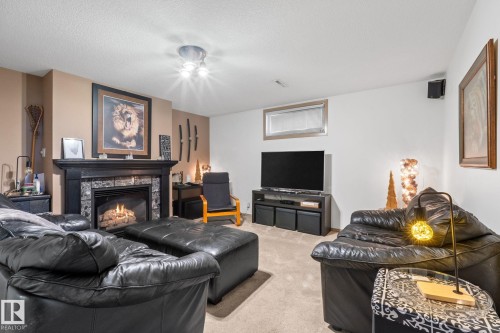 Living area featuring a central fireplace with a dark wood mantel and stone surround - 12115 53 Street, Edmonton, AB 
