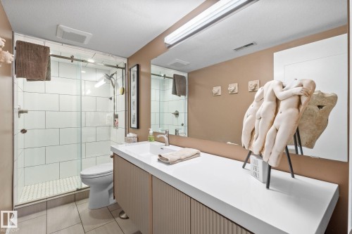 Bathroom featuring a glass-enclosed shower with white subway tile, a vanity with fluted paneling, a large integrated sink, and an expansive wall-mounted mirror - 12115 53 Street, Edmonton, AB 