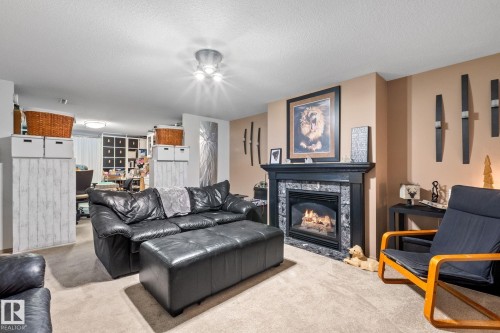 Living area featuring a gas fireplace with a dark wood mantel and a stone-tile surround - 12115 53 Street, Edmonton, AB 