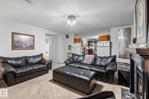 Carpeted living area featuring a built-in fireplace with a dark wood mantel and stone surround - 12115 53 Street, Edmonton, AB 