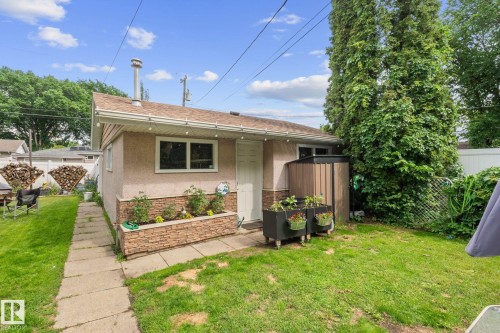 Backyard featuring a stucco exterior, stone veneer planter boxes, a shingled roof, a paved walkway, and mature landscaping - 12115 53 Street, Edmonton, AB 