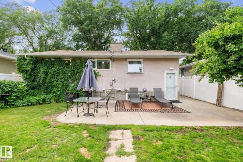 Expansive concrete patio area with a white privacy fence and a verdant backdrop of mature trees - 12115 53 Street, Edmonton, AB 