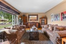 Bright living area featuring a large picture window, warm-toned walls, wood-finish flooring, and a textured area rug - 12115 53 Street, Edmonton, AB 