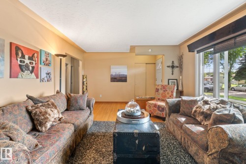 Spacious living area featuring light wood-finish flooring, ample natural light from a large window, neutral wall tones, and a built-in recessed light fixture - 12115 53 Street, Edmonton, AB 