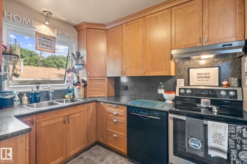Corner kitchen featuring light wood cabinetry, dark countertops, a double basin sink, and stainless steel appliances - 12115 53 Street, Edmonton, AB 
