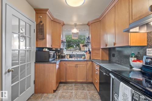 Kitchen featuring light wood-finish cabinetry, dark countertops, a black appliance suite, and a window above the sink - 12115 53 Street, Edmonton, AB 