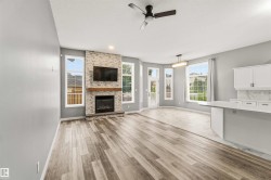 Spacious living area featuring wood-finish flooring, a stacked stone fireplace with a wood mantle, and numerous windows - 