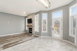 Open-concept living space featuring a tiled fireplace with a wood mantle, an array of tall windows, and a glass-paneled door - 