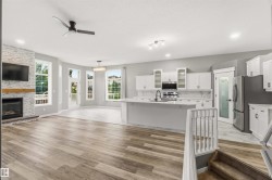 Open-concept living space featuring wood-finish flooring, a contemporary fireplace with a stone surround, and a kitchen with white cabinetry and an island - 