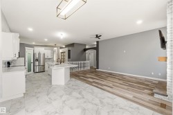 Contemporary kitchen and living area featuring white cabinetry, an island with an undermount sink, stainless steel appliances, and white marble-look tile flooring - 