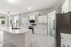 Kitchen featuring a large central island with a sink and matte black faucet, full suite of stainless steel appliances, white cabinetry with black hardware, and marble-look tile flooring - 