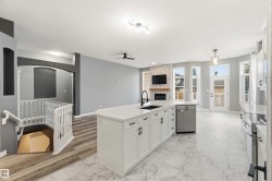 Contemporary kitchen featuring a large central island with a sink and modern faucet, white cabinetry with dark hardware, and a stainless steel dishwasher - 