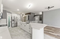 Open-concept kitchen featuring white cabinetry, a large center island with a black sink, stainless steel appliances, and marble-look tile flooring - 