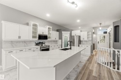 Spacious kitchen featuring an expansive island with an undermount sink and matte black faucet, white cabinetry with dark hardware, stainless steel appliances, and quartz countertops with a coordinated backsplash - 