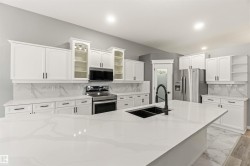 Contemporary kitchen featuring a large central island with a double basin sink and a matte black pull-down faucet - 