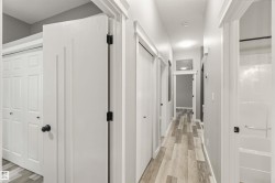 Hallway featuring wood-finish flooring, white doors with black hardware, and light gray walls - 
