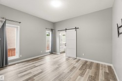 Spacious room featuring wood-finish flooring, light grey painted walls, two windows with white trim, and a white barn door leading to an interior space - 