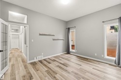 Spacious room featuring wood-finish flooring, light grey painted walls, two rectangular windows with opaque lower sections, and an entry door with frosted glass panels - 