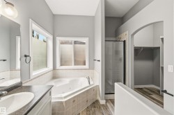 Corner soaking tub with tile surround, separate enclosed shower, and a single vanity with dark countertop - 