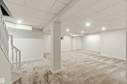 Spacious lower level featuring light-toned patterned carpeting, a grid-panel ceiling with recessed lighting, and crisp white walls - 