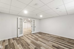 Spacious room featuring wood-finish flooring, white walls, and a dropped ceiling with integrated lighting - 