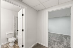 Interior hallway featuring a bathroom with wood-finish flooring and a white toilet, and an additional room with gray carpet - 