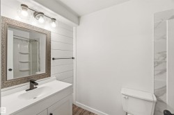 Bathroom featuring a white vanity with an integrated sink, a rectangular framed mirror, and a wall-mounted light fixture with three clear glass shades - 