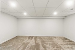 Spacious room featuring neutral-toned carpeting, white painted walls, and a drop ceiling with recessed lighting - 