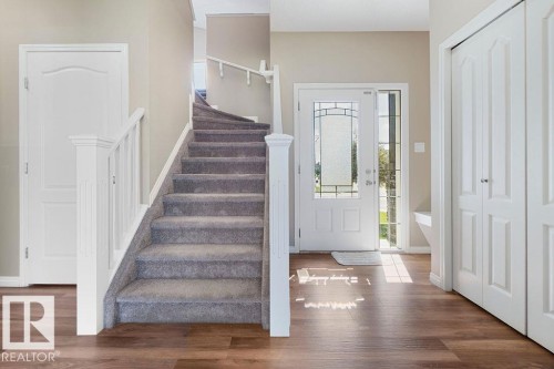 Inviting entryway featuring wood-finish flooring, a carpeted staircase with white railings, a front door with decorative glass inserts and sidelight, two-panel interior doors, and bi-fold closet doors - 1306 32A Street, Edmonton, AB 