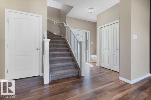 Inviting entryway featuring wood-finish flooring, a carpeted staircase with white railings, a white paneled door, and a white bi-fold closet door - 1306 32A Street, Edmonton, AB 