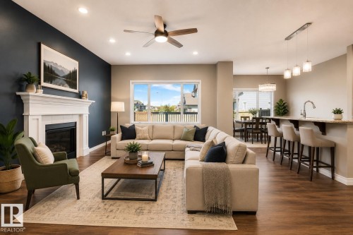 Open-concept living area featuring wood-finish flooring throughout, a white mantel fireplace with a dark hearth, and recessed lighting - 1306 32A Street, Edmonton, AB 