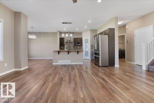 Open-concept living area featuring wood-finish flooring, a kitchen island with seating, stainless steel appliances, dark cabinetry, and recessed lighting - 1306 32A Street, Edmonton, AB 