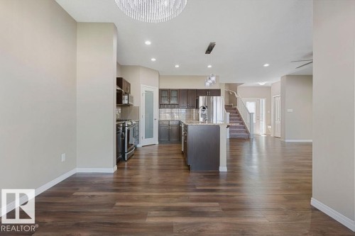Open-concept living area with wood-finish flooring, a contemporary kitchen, stainless steel appliances, and a central island with a stone-finish countertop - 1306 32A Street, Edmonton, AB 
