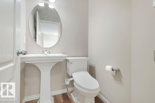Pedestal sink with chrome faucet, oval mirror, and wall-mounted light fixture - 1306 32A Street, Edmonton, AB 