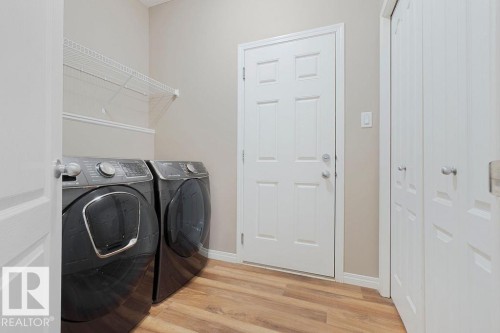 Dedicated laundry area featuring wood-finish flooring, light neutral wall paint, and overhead wire shelving - 1306 32A Street, Edmonton, AB 