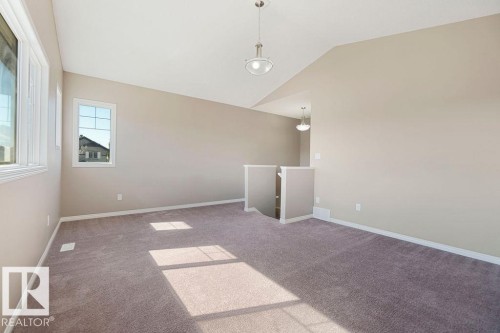 Spacious room featuring neutral carpeting, multiple windows, and a ceiling pendant light fixture - 1306 32A Street, Edmonton, AB 